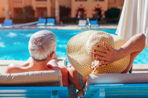 Senior couple relaxing by swimming pool lying on chaise-longues. People enjoying summer vacation. Senior family couple relaxing by swimming pool lying on chaise-longues. People enjoying summer vacation. chaise longue stock pictures, royalty-free photos & images