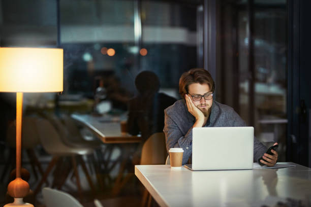 Watching the clock doesn't get work done Shot of a young businessman looking bored while using a laptop during a late night at work wasting time stock pictures, royalty-free photos & images