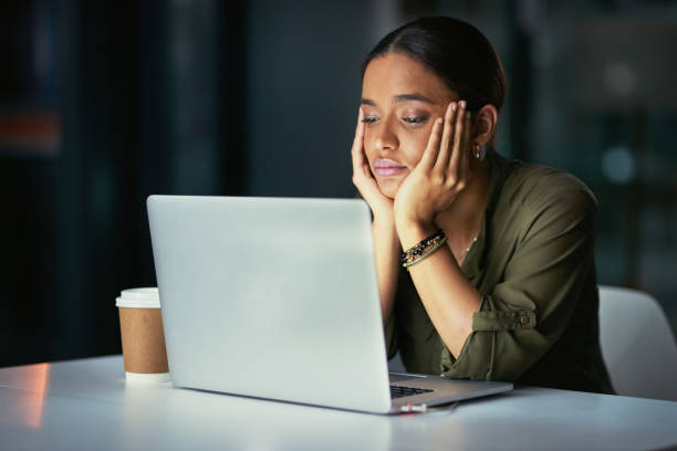 Why do I do this to myself? Shot of a young businesswoman looking bored while using a laptop during a late night at work wasting time stock pictures, royalty-free photos & images