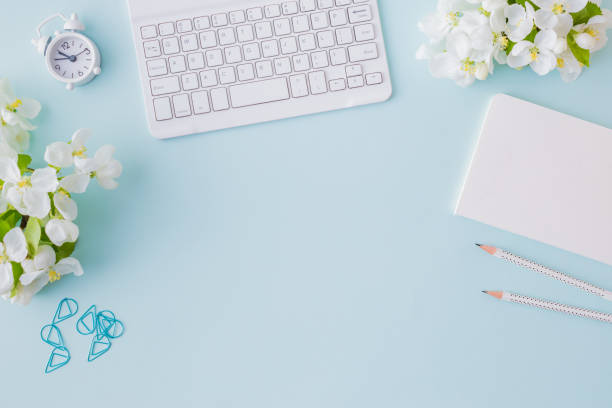 istock Flat lay blogger or freelancer workspace with a notebook, keyboard and white spring flowers on a blue background 1146069295