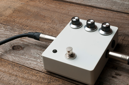Blank white guitar pedal with vintage knobs and plugged jacks on the floor
