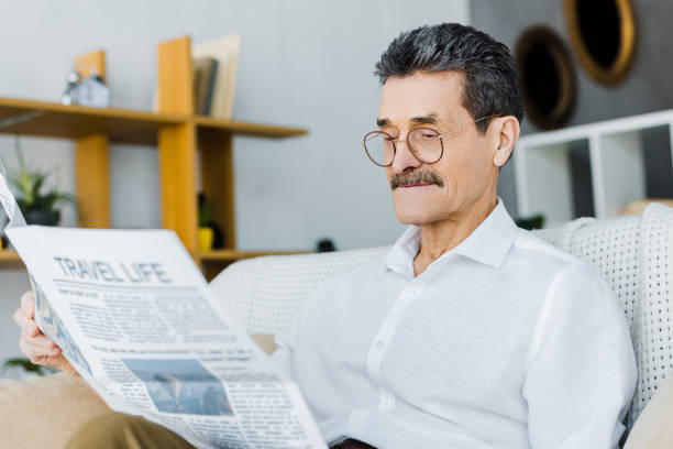 istock cheerful senior man in glasses reading travel newspaper while sitting on sofa 1146072832
