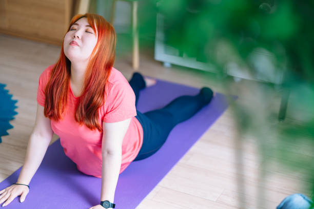 Young woman doing yoga at home A young woman is doing yoga at home. plus size photos stock pictures, royalty-free photos & images