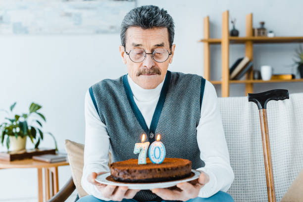 istock sad senior man holding birthday cake while sitting on sofa a in living room 1146074604