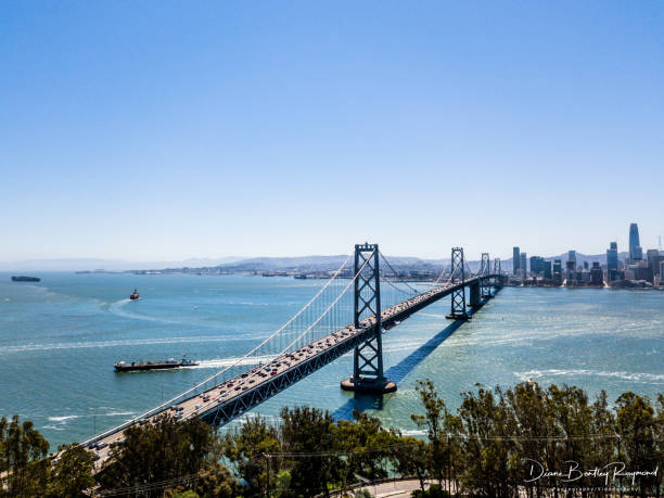 An aerial view of the Bay Bridge on a sunny day. A view from Treasure Island looking across the bay at the San Francisco Skyline. Ships and boats are in the Bay.