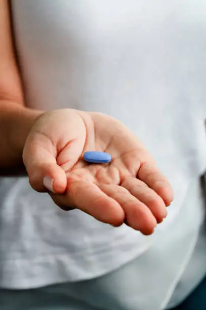 Health themes. Young woman hands offering a single blue pill