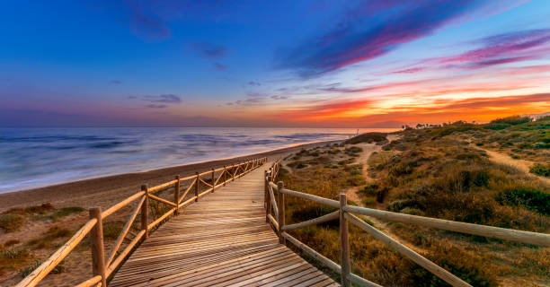Bright sunset sky over sea and timber path View of amazing bright sundown sky over waving sea and wooden path in countryside in Cabopino, Artola dunes. Marbella, Spain costa del sol málaga province photos stock pictures, royalty-free photos & images