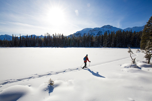 A woman goes for a snowshoe adventure across a small frozen lake in the Rocky Mountains of Canada.