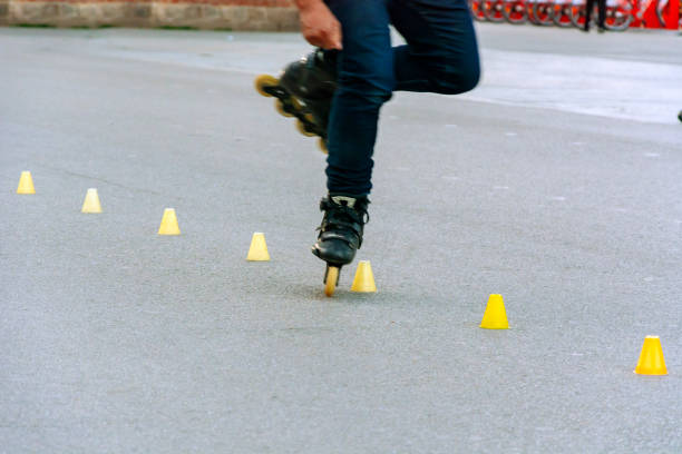 Feet of a skater while performing the slalom between yellow plastic cones placed in line on the asphalt