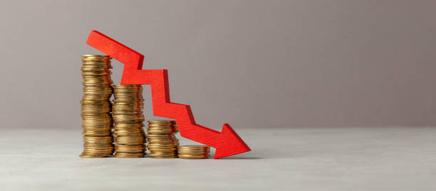 Green arrow down over stack of coins by ladder on gray background. Copy space for text. stock photo