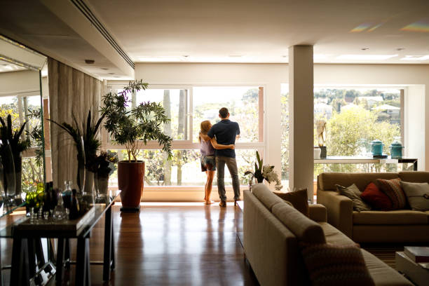 pareja admirando la vista desde la sala de estar de su casa. - edificio residencial fotografías e imágenes de stock