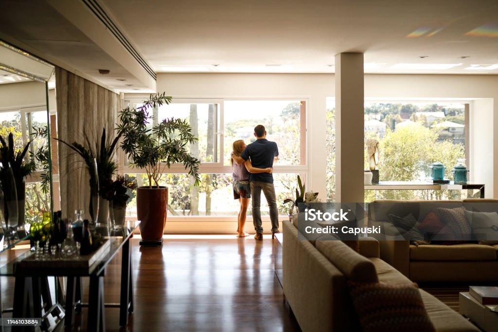 Couple admiring the view from the living room of their house. Domestic Life Stock Photo