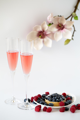 Two glasses of rose sparking wine with berries and flowers on white background