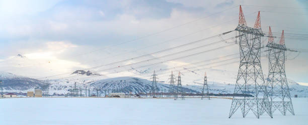 High voltage towers with blue sky and snowy mountains background stock photo