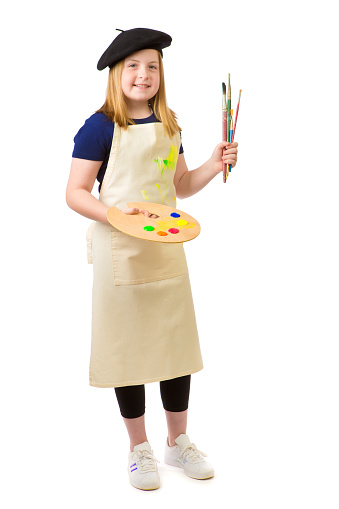 Young girl career aspiration of becoming an artist painter. She is holding a paint pallette and paint brushes.