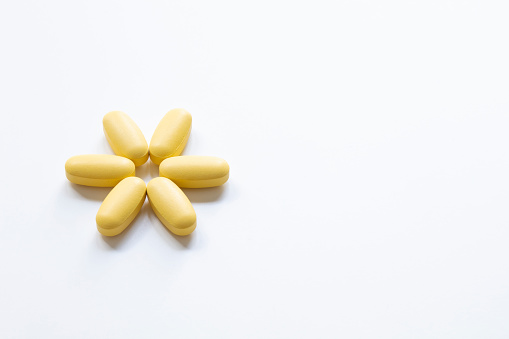 Yellow pharmacological medicine pills for medical treatments arranged in flower pattern isolated on white