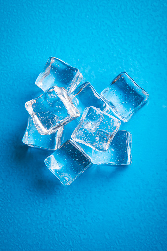 An overhead view of ice cubes on a blue and wet surface.