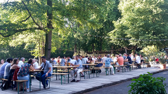 Berlin, Germany - May 28, 2018: People getting together at the end of a hot day in summer in one of the beer garden downtown.  Meeting each other, drinking beer and having a snack till dusk is falling.