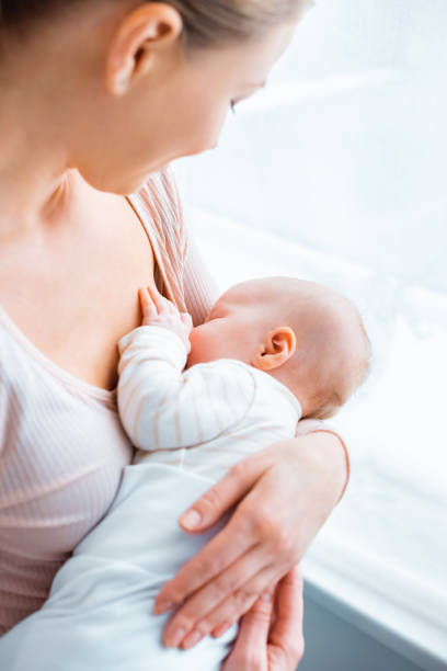 cropped shot of young mother breastfeeding adorable baby at home stock photo