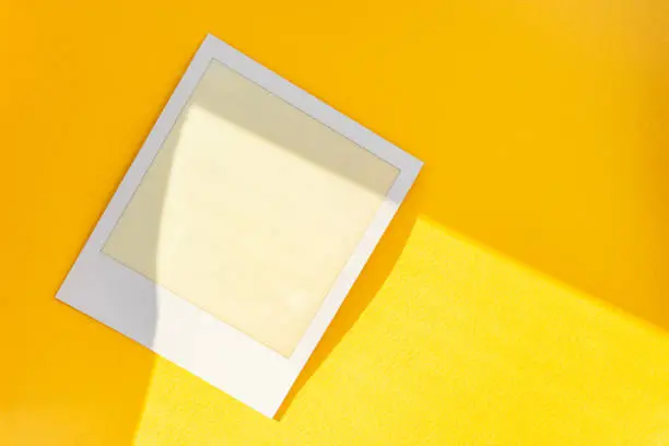 Photo of white and empty but exposed instant film frame on yellow paper background