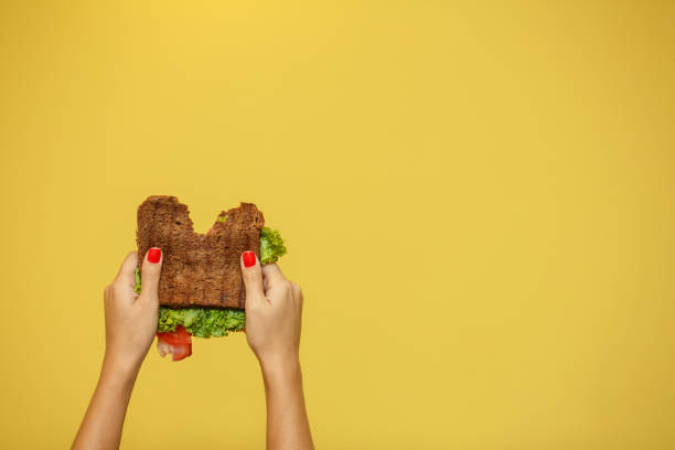 女性の手は黄色の背景に噛まサンドイッチを保持します。サンドイッチプロモーションコンセプト