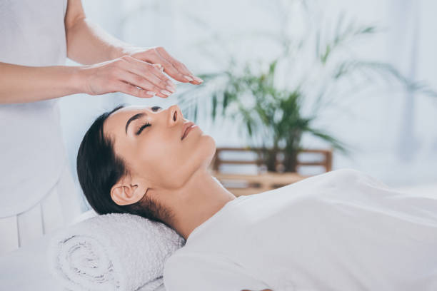 cropped shot of calm young woman with closed eyes receiving reiki treatment above head stock photo