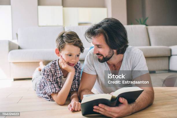 Boys Are Lying On The Floor Man Holds Book And Look At Son He Smiles To Him Boy Is Shy He Hols Hand On Face Stock Photo - Download Image Now