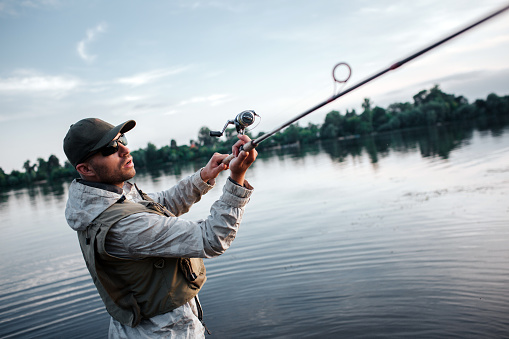 Fisherman in action. He holds fly rod witth both hands. Guy is trying to catch salmon. He is serious and concentrated