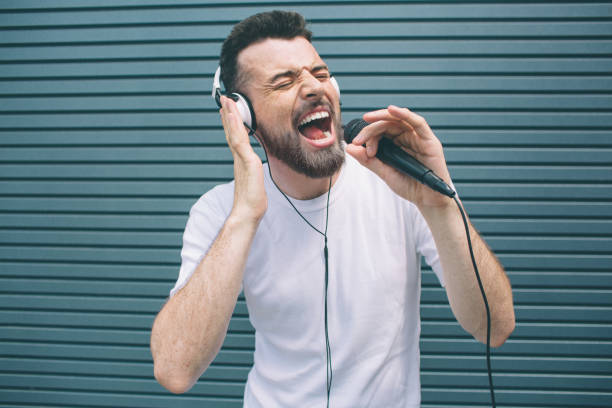 il musicista felice si diverte ad ascoltare musica. indossa le cuffie e canta. il ragazzo sta usando il karaoke. l'uomo canta ad alta voce. isolato su sfondo a strisce e blu. - instrumental hip hop immagine foto e immagini stock