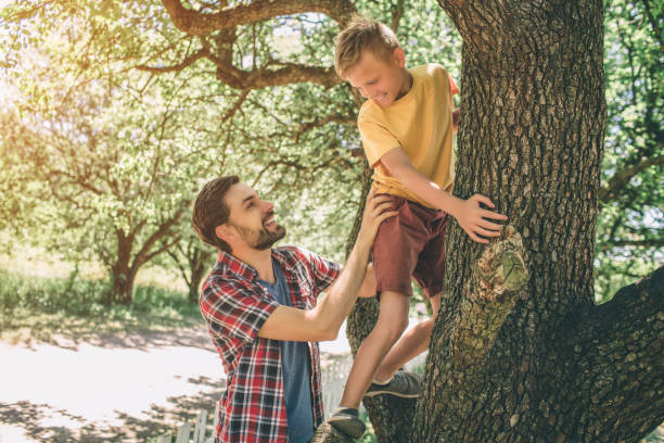 istock Father and son are playing with each other. Guy is supporting his child. Boy is looking down at father. They are smiling. Both of them are happy. 1146125261