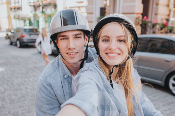 beau couple est assis sur les sièges de la moto et la recherche sur la caméra. la fille tient la caméra. elle prend du selfie. ils sourient. - motorcycle motor scooter couple young adult photos et images de collection