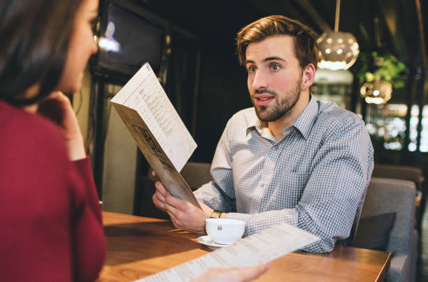 o homem e a mulher estão sentando-se no restaurand e estão prendendo algum menu. eles querem deside o que a ordem para comer lá. o homem está dando alguns conselhos de comida para a mulher. - deside - fotografias e filmes do acervo