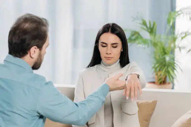 bearded hypnotist holding wrist of young woman with closed eyes during hypnotherapy