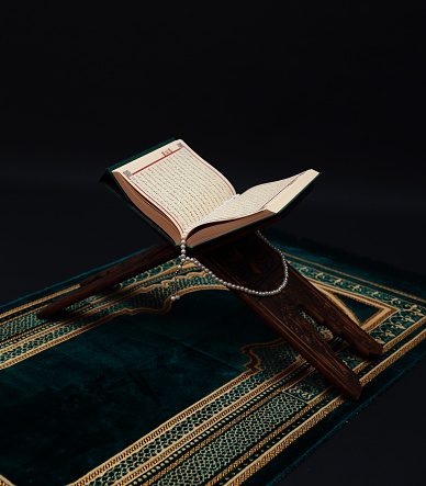 Libro sagrado islámico Corán sobre tallado de madera rahle con abalorios de Rosario y alfombra de oración sobre fondo negro. Kuran el libro sagrado de los musulmanes. Concepto de Ramadán. photo