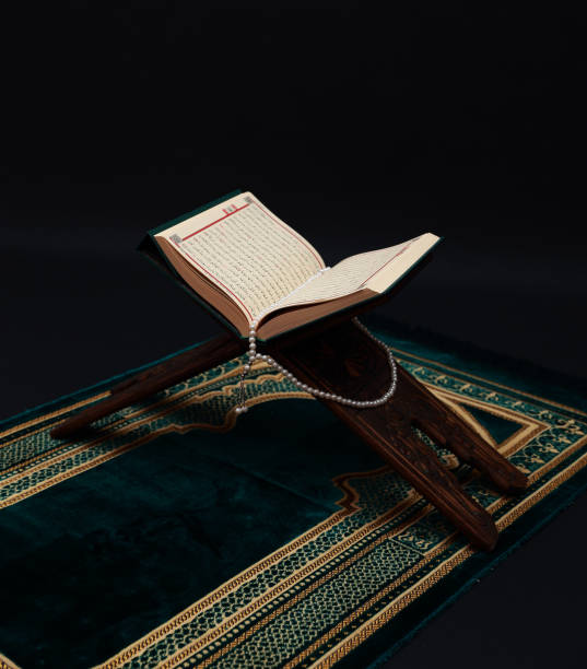 Islamic Holy Book Quran on wood carving rahle with rosary beads and prayer rug on black background. Kuran the holy book of Muslims. Ramadan concept. Islamic Holy Book Quran on wood carving rahle with rosary beads and prayer rug on black background. Kuran the holy book of Muslims. Ramadan concept. koran photos stock pictures, royalty-free photos & images