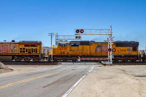 Barstow, CA / USA – April 14, 2019: Union Pacific freight train moving pass Hinkley Road in the Mojave Desert near the city of Barstow, California with gates down and red flashing signal lights.