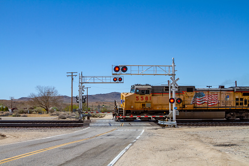 Barstow, CA / USA – April 14, 2019: Union Pacific freight train moving pass Hinkley Road in the Mojave Desert near the city of Barstow, California with gates down and red flashing signal lights.