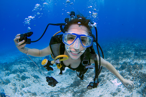 female scuba diver, using a blue mask, holding the regulator on one hand and smiling to the camera on a deep blue ocean, in Mexico (Cozumel island).