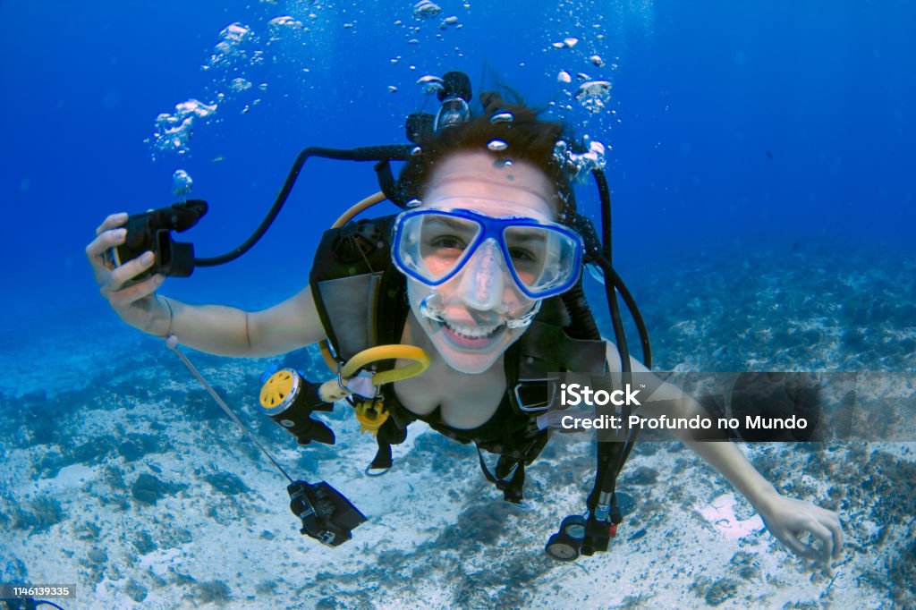 Woman scuba diver smiling underwater female scuba diver, using a blue mask, holding the regulator on one hand and smiling to the camera on a deep blue ocean, in Mexico (Cozumel island). Scuba Diving Stock Photo