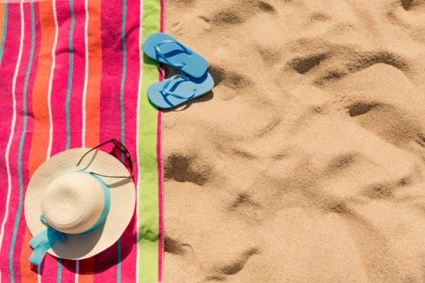 Beach towel with beach accessories on sandy tropical beach top view with copy space