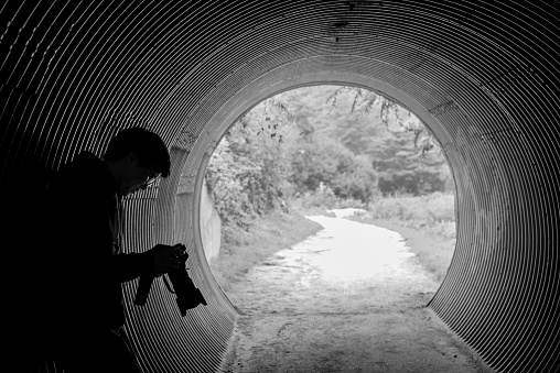 Asian man with glasses holding DSLR camera leaning in the tunnel. Travel photography concept