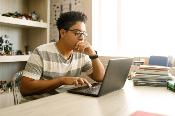 adolescent étudiant avec l’ordinateur portatif à la maison - jeunes garçons photos et images de collection