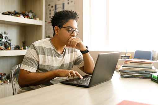 Teenage boy studying with laptop at home.