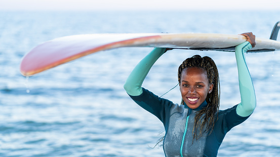 Smiling african woman holding a surfboard over her head.