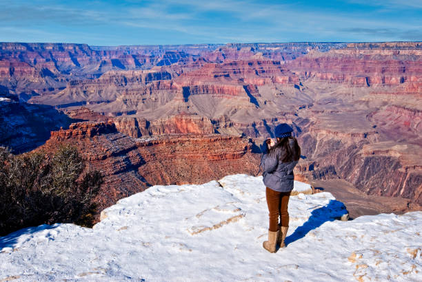 Grand Canyon National Park, Arizona, USA - January 01, 2013: A young woman, standing in the snow, is photographing the Grand Canyon with a smart phone. This picture was taken from Yavapai Point.
