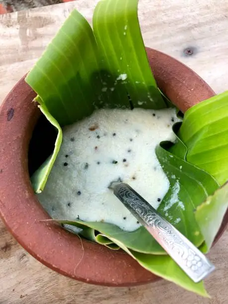 Photo showing a traditional South Indian coconut chutney curry / pickle, which has just been made and is being served as a tasty breakfast, together with some dosas / savoury pancakes. This delicious homemade coconut chutney recipe was photographed at a beachfront homestay guesthouse hotel in Kollam, Kerala, South India, being served in rustic unglazed clay dish and made using black peppercorns, green chillies, while underneath the pickle is a tropical green banana leaf and an ornate silver spoon in the mixture itself.