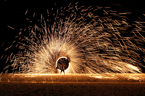 Traditional spectacular spinning illuminate torch fireball Thai fire show on the island beach at night
