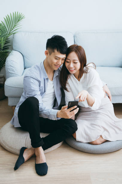 istock Happy young couple using smartphone while relaxing in living room 1146196537