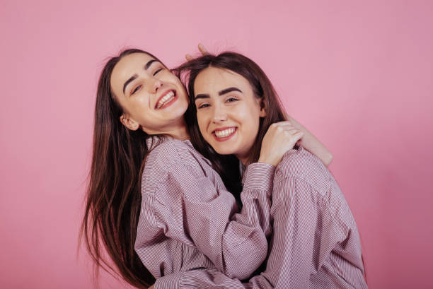 oprechte emoties. twee zussen tweeling staande en poseren in de studio met witte achtergrond - eeneiige tweeling stockfoto's en -beelden