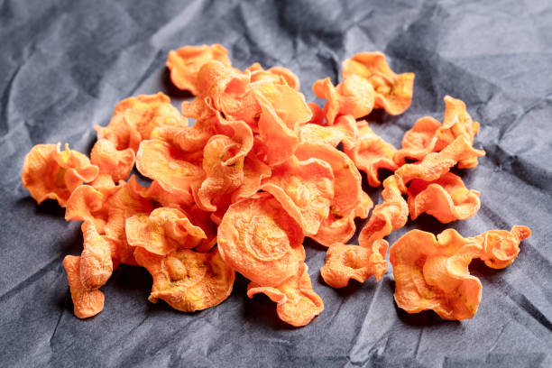 small pile of orange  carrot chips  on rumpled black wrapping paper. - root paper black textured imagens e fotografias de stock